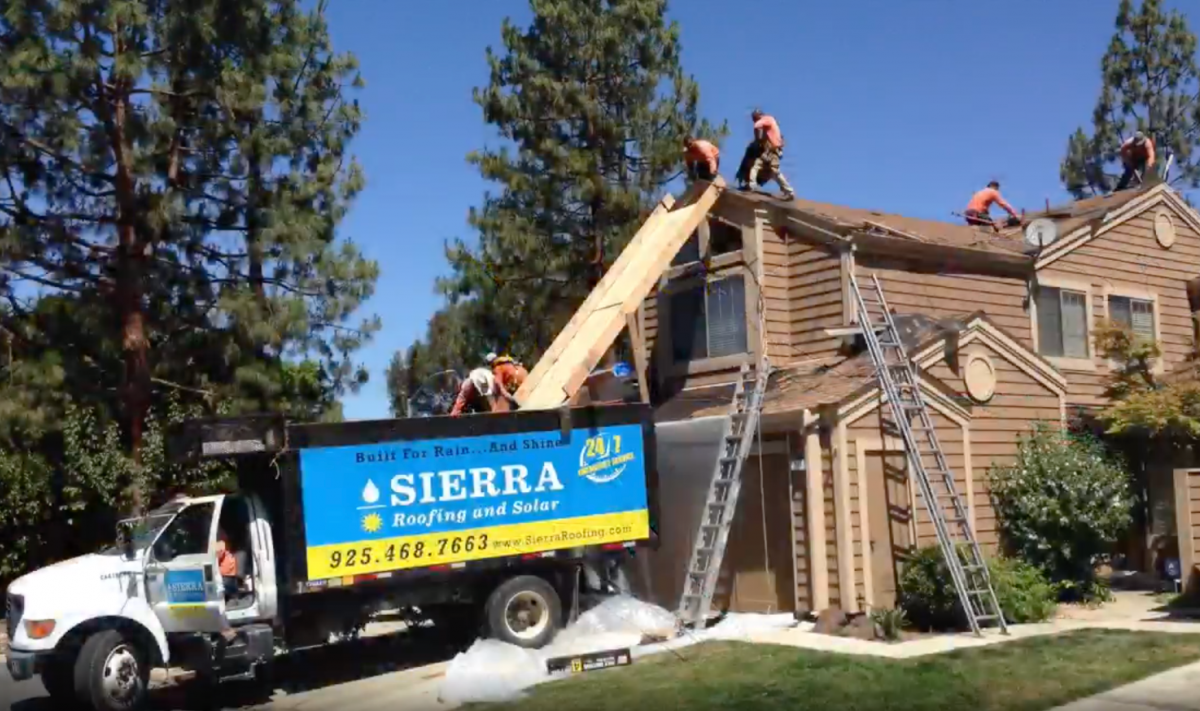 Workers replace a roof, using a dump truck to dispose of old materials